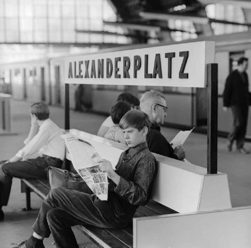 Boy reading a newspaper on a bench in the station Alexanderplatz in Berlin - Mitte