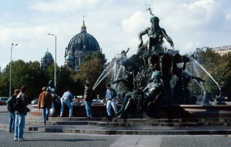 A group of teenagers refreshed on Neptune Fountain in Berlin - Mitte. In the background of the Berlin cathedral is seen. From a basic dish on a three-tier base, the powerful figure of the ancient Roman sea god Neptune rises