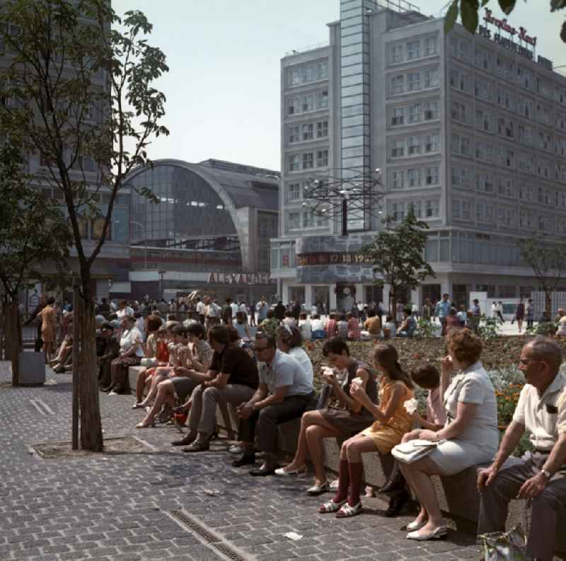 Tourists sitting on the world clock in front of the S-train station Alexanderplatz in Berlin - Mitte. In the right background is the Berolina house to see