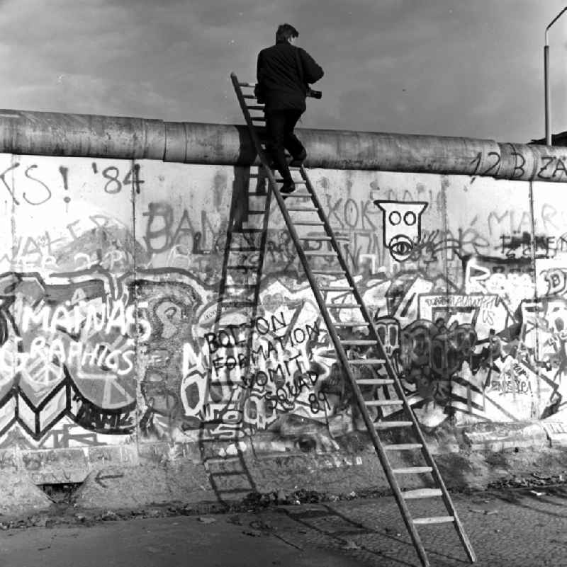 Curious climbs a photographer on a ladder at the Berlin Wall up