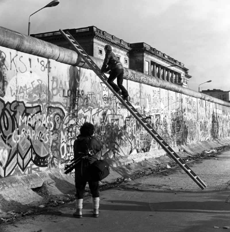 Curious onlookers climb on a ladder at the Berlin Wall up