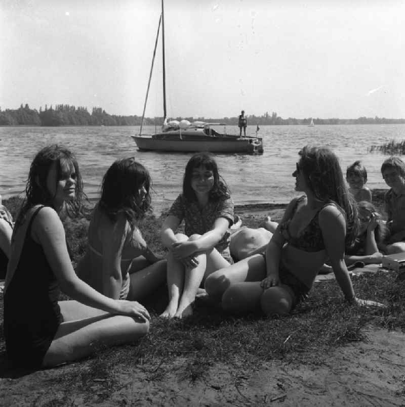 Campingurlaub am Krossinsee. Urlauber beim Baden und Sonnen. Eine Gruppe junger Frauen posiert für die Kamera. Im Hintergrund wird ein Segelboot zum Auslaufen klar gemacht.