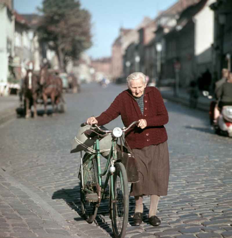 Eine alte Frau schiebt ihr beladenes Fahrrad über eine Kopfsteinpflasterstraße in Bernau.