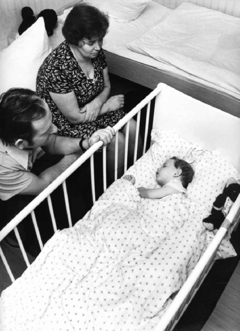 Parents sit in the cot of her sleeping child in Boxberg/Oberlausitz in the state Saxony on the territory of the former GDR, German Democratic Republic