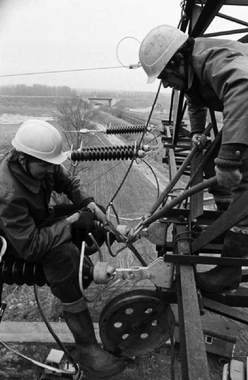 Arbeiter bei der Montage einer Hochspannungsleitung bei Brieselang in luftiger Höhe in Aktion. Die DDR-Energieversorung basiert zu einem großen Teil auf der Verstromung von Braunkohle aus der Lausitz und Sachsen, was unter anderem lange Leitungswege nötig macht.