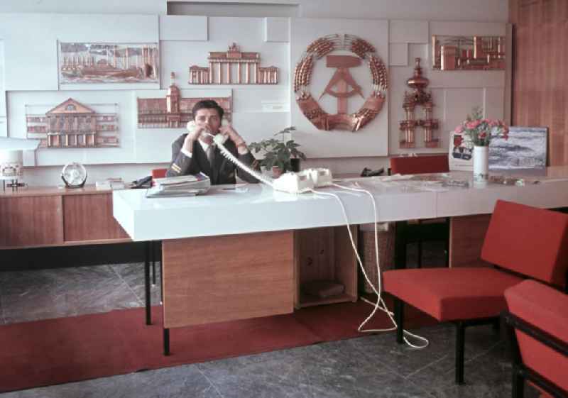 Ein Angestellter telefoniert in der Vertretung der DDR-Fluggesellschaft Interflug in der ungarischen Hauptstadt Budapest mit zwei Telefonen gleichzeitig. Im Hintergrund die verschiedenen kulturellen Sehenswürdigkeiten der DDR.