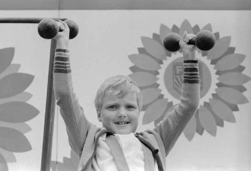 A little boy with two dumbbells made of metal at the Whitsun meeting of the FDJ in Karl-Marx-Stadt, today Chemnitz in the federal state Saxony on the territory of the former GDR, German Democratic Republic