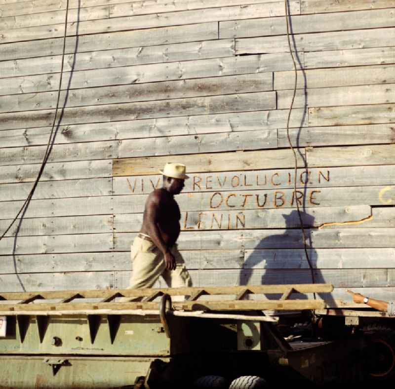 Arbeiter in einer Düngemittelfabrik in Cienfuegos. An der Bretterwand steht die Aufschrift 'Viva Revolucion Octubre Lenin'. In den 60er und 7