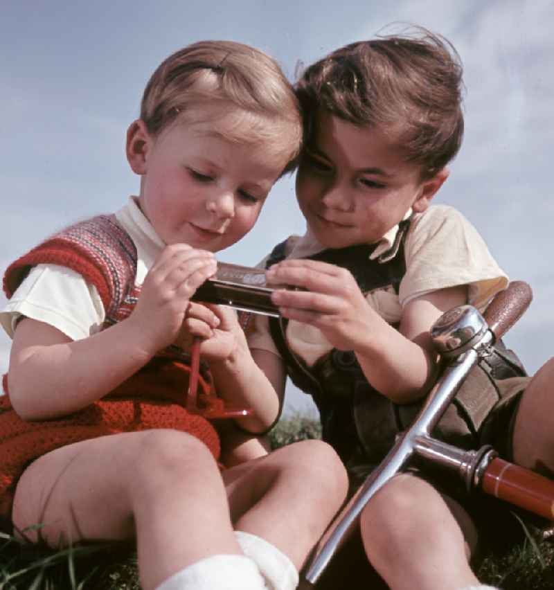 Two boys play with a harmonica and a scooter in Coswig, Saxony in the territory of the former GDR, German Democratic Republic