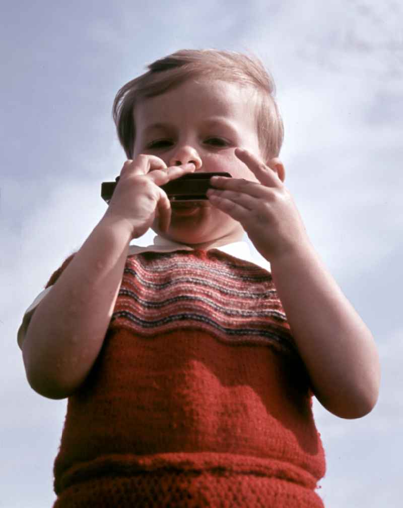 A little boy plays a harmonica in Coswig, Saxony in the territory of the former GDR, German Democratic Republic