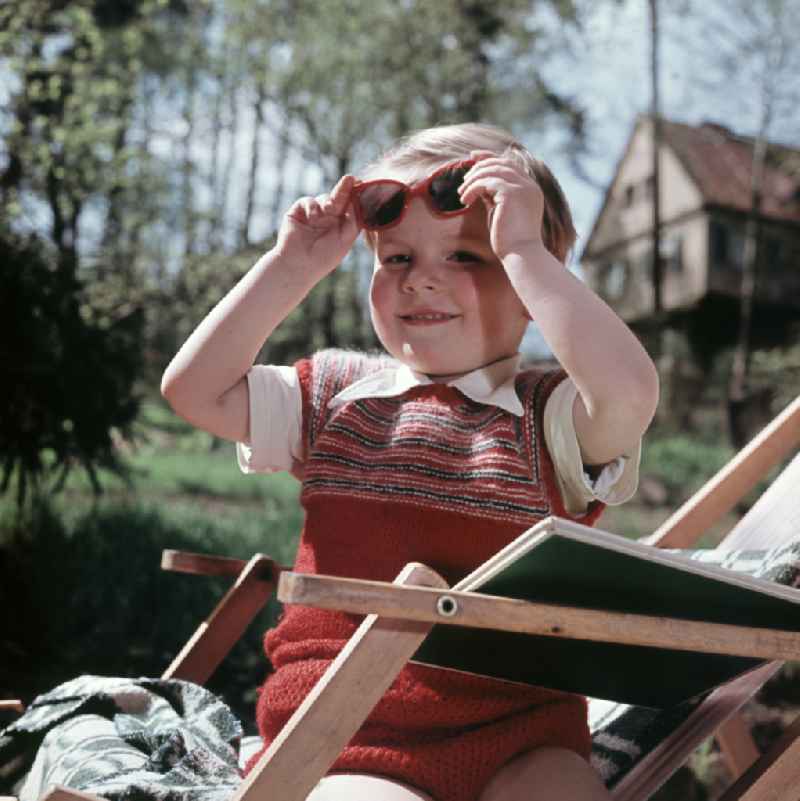 A boy sits on a deck chair with a book and sunglasses in Coswig, Saxony in the territory of the former GDR, German Democratic Republic
