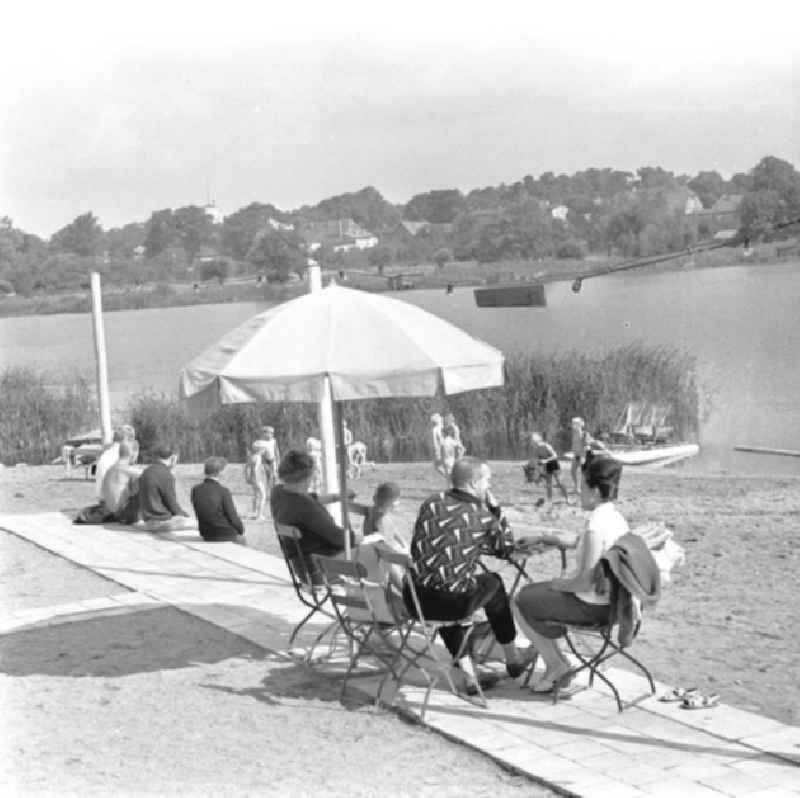 Am Ufer vom Klostersee sitzen Menschen / Passanten / Einwohner am Tisch unterm Sonnenschirm zusammen.