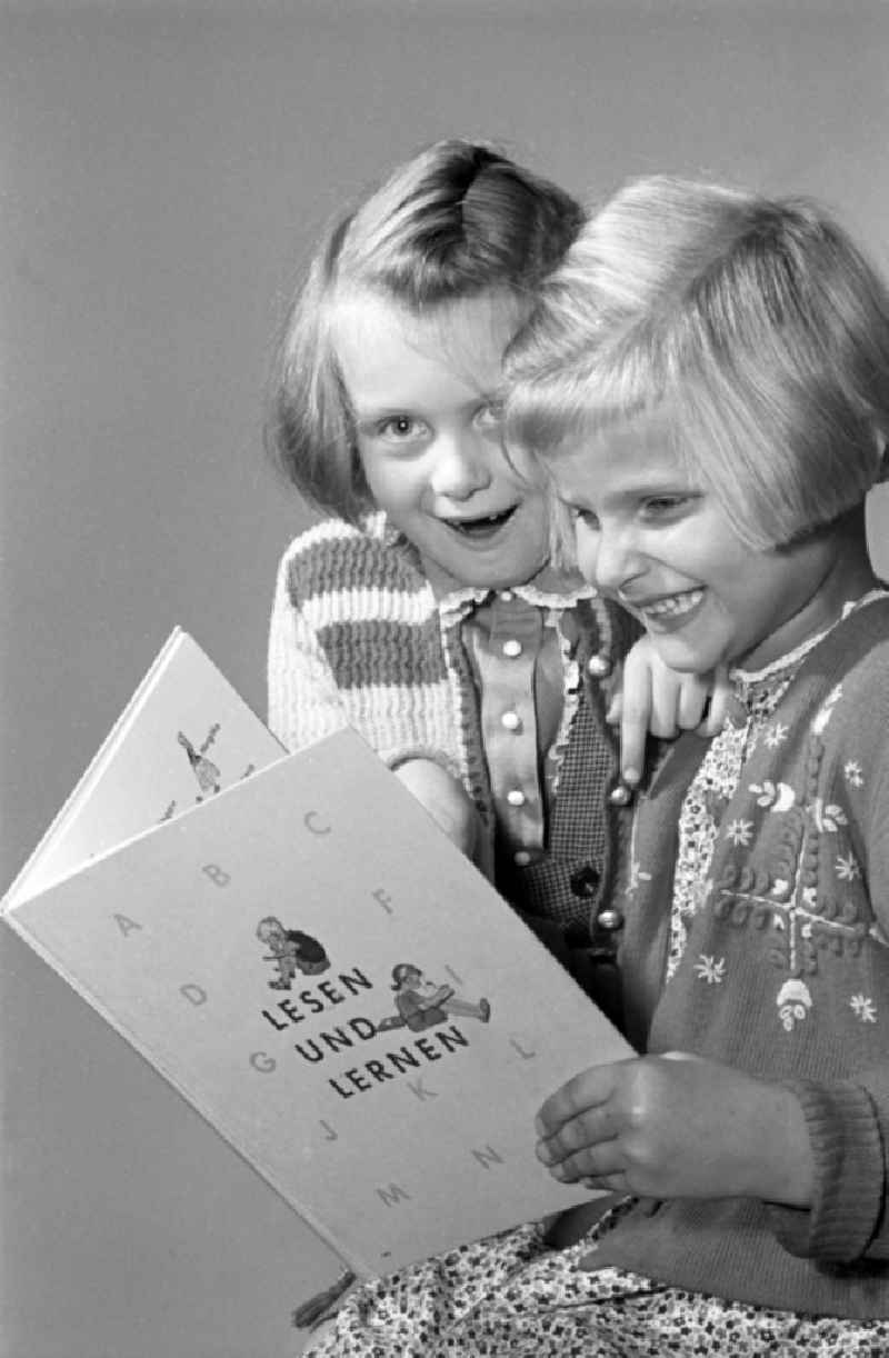 Children on the occasion of the start of school for two young girls enthusiastically looking at a school book on the German language 'Unsere Fiebel' in the district of Altstadt in Dresden in the state of Saxony on the territory of the former GDR, German Democratic Republic