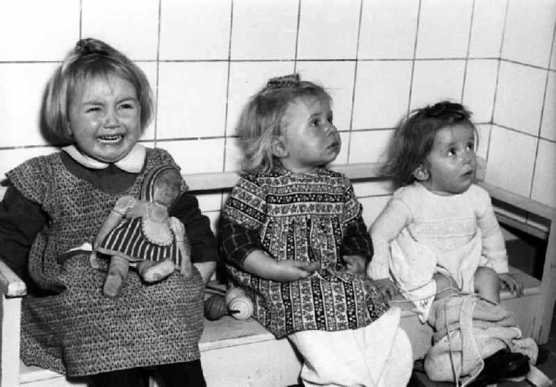 Fun and games for small children cared for by educators in a kindergarten on a bench in Dresden in the state of Saxony in the area of the former GDR, German Democratic Republic
