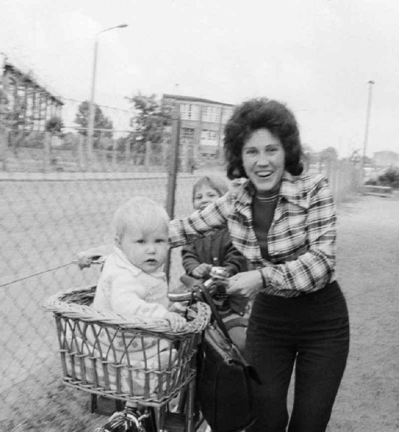 A woman with two children and bicycle in Eberswalde in Brandenburg on the territory of the former GDR, German Democratic Republic. A toddler sitting in a bicycle basket willow rods and the other on the carrier from the bike