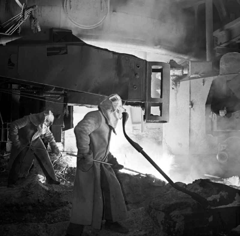 Zwei Arbeiter in Schutzanzügen beim Verrichten ihrer Tätigkeit im Eisenhüttenkombinat Ost (EKO) in Eisenhüttenstadt. Am 18. August 195