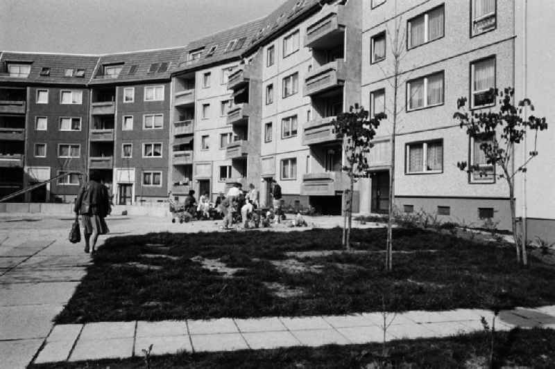 Blick in den Innenhof eines Neubaugebietes mit Plattenbauten im Hintergrund. Eltern mit ihren Kindern spielen zusammen auf dem Spielplatz.
