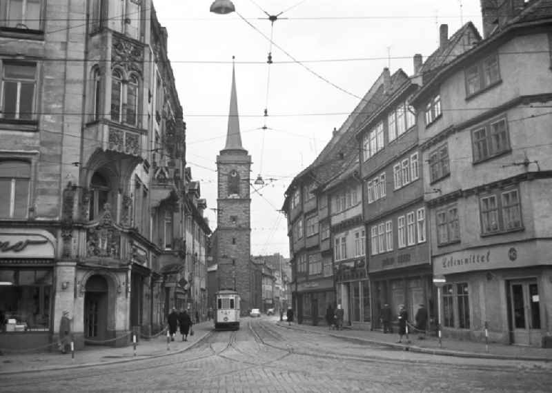 Straßenszene in der Erfurter Innenstadt - Marktstraße mit einigen Geschäften und ein HO-Lebensmittelladen. Im Hintergrund ist der Westturm der Allerheiligenkirche zu sehen. Außerdem im Bild einige Passanten und eine Tram. Bestmögliche Qualität nach Vorlage!