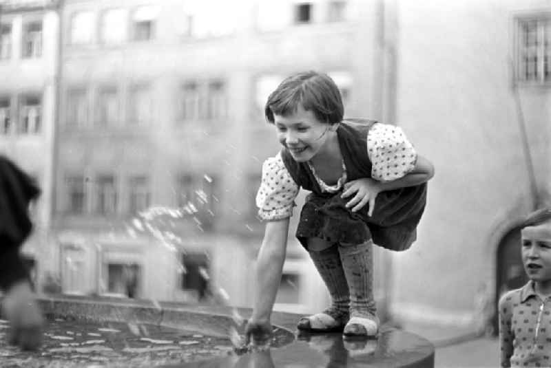 Ein Mädchen plantscht lachend mit der Hand in einem Springbrunnen in Freiberg.