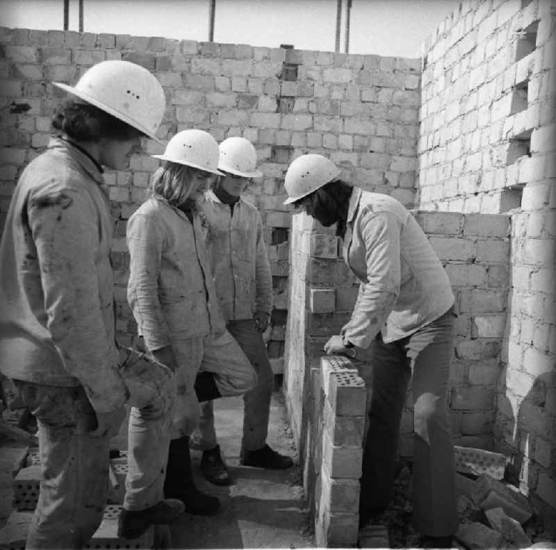 Drei Maurerlehrlinge beim praktischen Unterricht mit Ausbilder auf Baustelle.