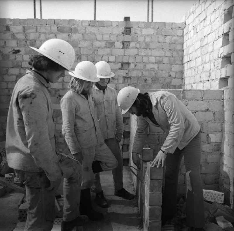 Drei Maurerlehrlinge beim praktischen Unterricht mit Ausbilder auf Baustelle.