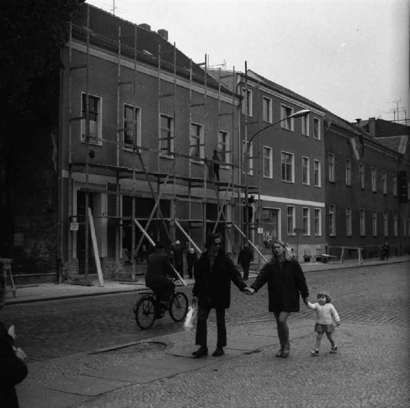Alltagsszene / Stadtansicht. Eine junge Familie geht spazieren, ein Fahrradfahrer fährt auf der Strasse und  Bauarbeiter demontieren ein Baugerüst im Hintergrund.