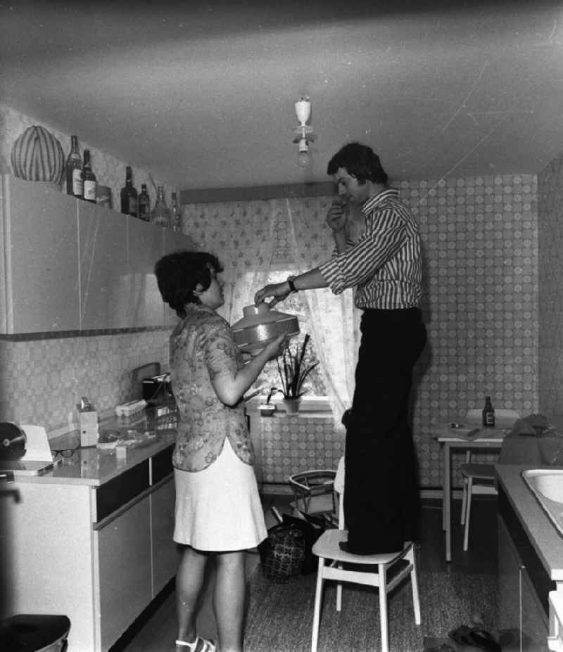 Küche in der Neubauwohnung einer jungen Familie im Stil der siebziger Jahre. Ein junges Paar wechselt die Glühbirne der Küchen-Leuchte.