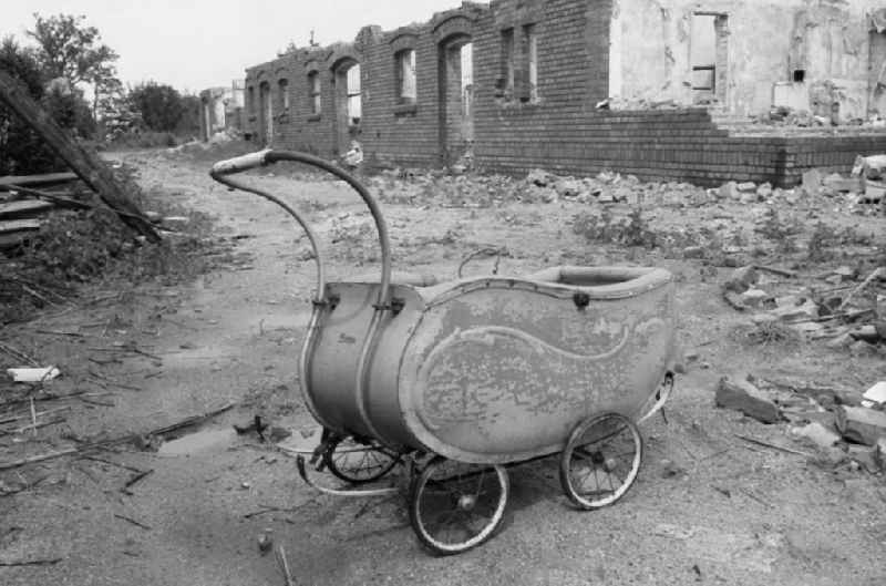 An old basket stroller stands on the street in front of a ruin during demolition work on cleared and depopulated areas to expand the opencast mine for mining brown coal - ruins in Gross-Luebbenau Spreewald, Brandenburg on the territory of the former GDR, German Democratic Republic