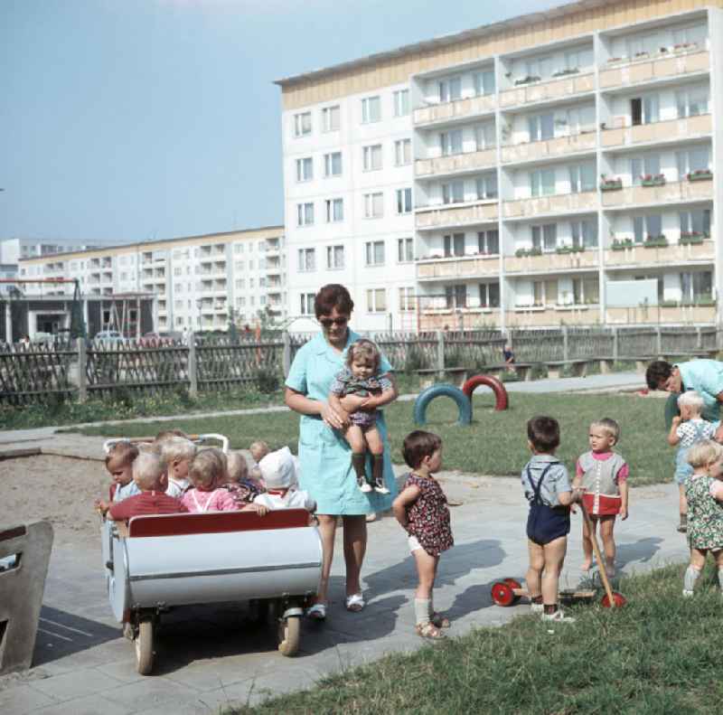 Eine Erzieherin trägt ein kleines Kind zu einem Kinderwagen in einem Kindergarten in Halle-Neustadt. Am Standort der Chemieindustrie der DDR wurde in den 1960er und 197