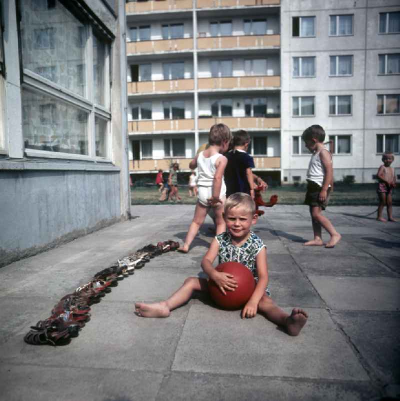 Ein Kind aus einem Kindergarten in Halle-Neustadt sitzt mit einem Ball vor einer Reihe Schuhe. Am Standort der Chemieindustrie der DDR wurde in den 1960er und 197