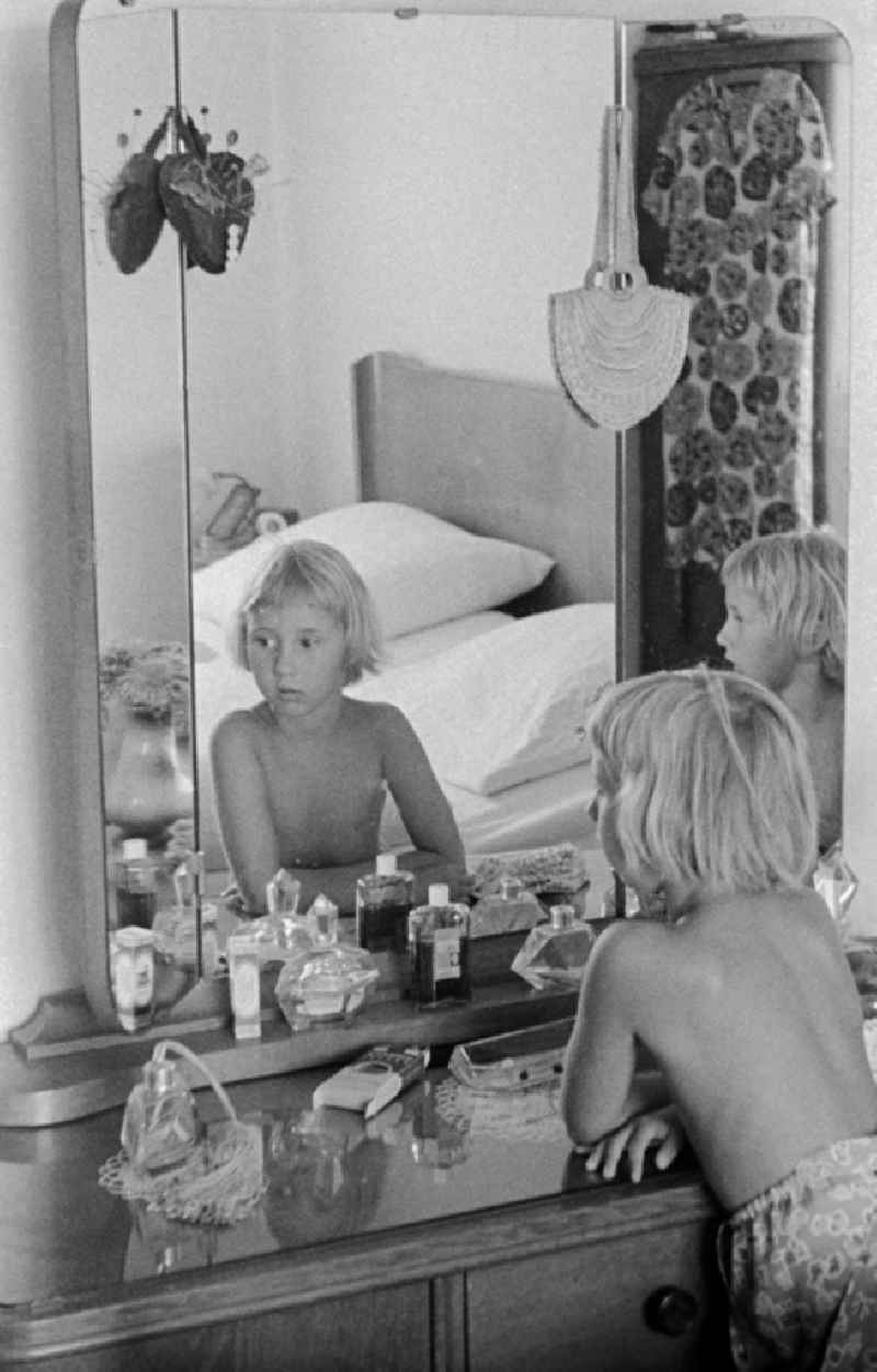 Two children stand before a dressing table with 3-part mirror, glass top and different perfume bottles in a bedroom in hall (hall) in the federal state Saxony-Anhalt on the area of the former GDR, German democratic republic