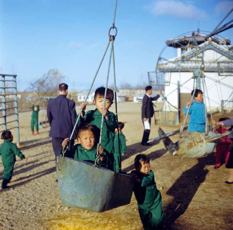 Kinder in 'Einheitsanzügen' spielen auf einem Spielplatz in einem LPG-Kindergarten nahe der Hafenstadt Hamhung in der Koreanischen Demokratischen Volksrepublik KDVR.