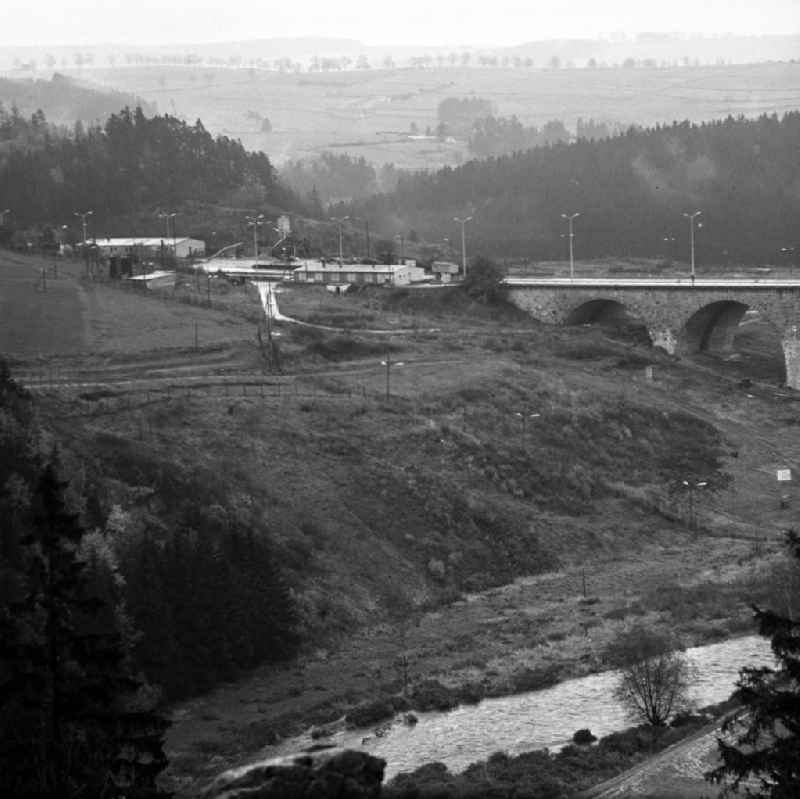Blick auf die Autobahnbrücke über die Saale zwischen Hirschberg (Thüringen) und Rudolphstein (Bayern). Die Brücke war am Ende des Zweiten Weltkrieges stark beschädigt, ein Bogen im April 1965 gesprengt worden. Die Instandsetzung erfolgte nach einem Vertrag zwischen der DDR und der BRD, die die Finanzierung des Baus übernahm. Im Hinterland der DDR wurden die Abfertigungsgebäude für die Grenzübergangsstelle (GÜST) Hirschberg errichtet, der Autobahn-Grenzübergang im Dezember 1966 eröffnet. Nach der Wiedervereingung erfolgte der Rückbau der Anlagen und die Erweiterung der Brücke durch den dreispurigen Ausbau der A9. Sie heißt heute auch 'Brücke der Deutschen Einheit'.