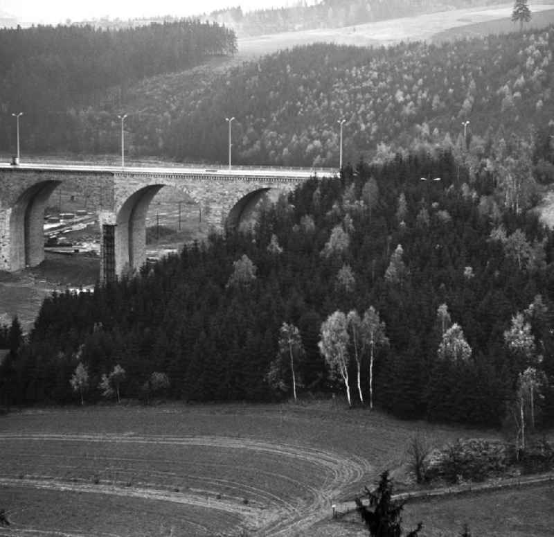 Blick auf den wiederaufgebauten Teil der Autobahnbrücke über die Saale zwischen Hirschberg (Thüringen) und Rudolphstein (Bayern). Die Brücke war am Ende des Zweiten Weltkrieges stark beschädigt, ein Bogen im April 1965 gesprengt worden. Die Instandsetzung erfolgte nach einem Vertrag zwischen der DDR und der BRD, die die Finanzierung des Baus übernahm. Im Hinterland der DDR wurden die Abfertigungsgebäude für die Grenzübergangsstelle (GÜST) Hirschberg errichtet, der Autobahn-Grenzübergang im Dezember 1966 eröffnet. Nach der Wiedervereingung erfolgte der Rückbau der Anlagen und die Erweiterung der Brücke durch den dreispurigen Ausbau der A9. Sie heißt heute auch 'Brücke der Deutschen Einheit'.