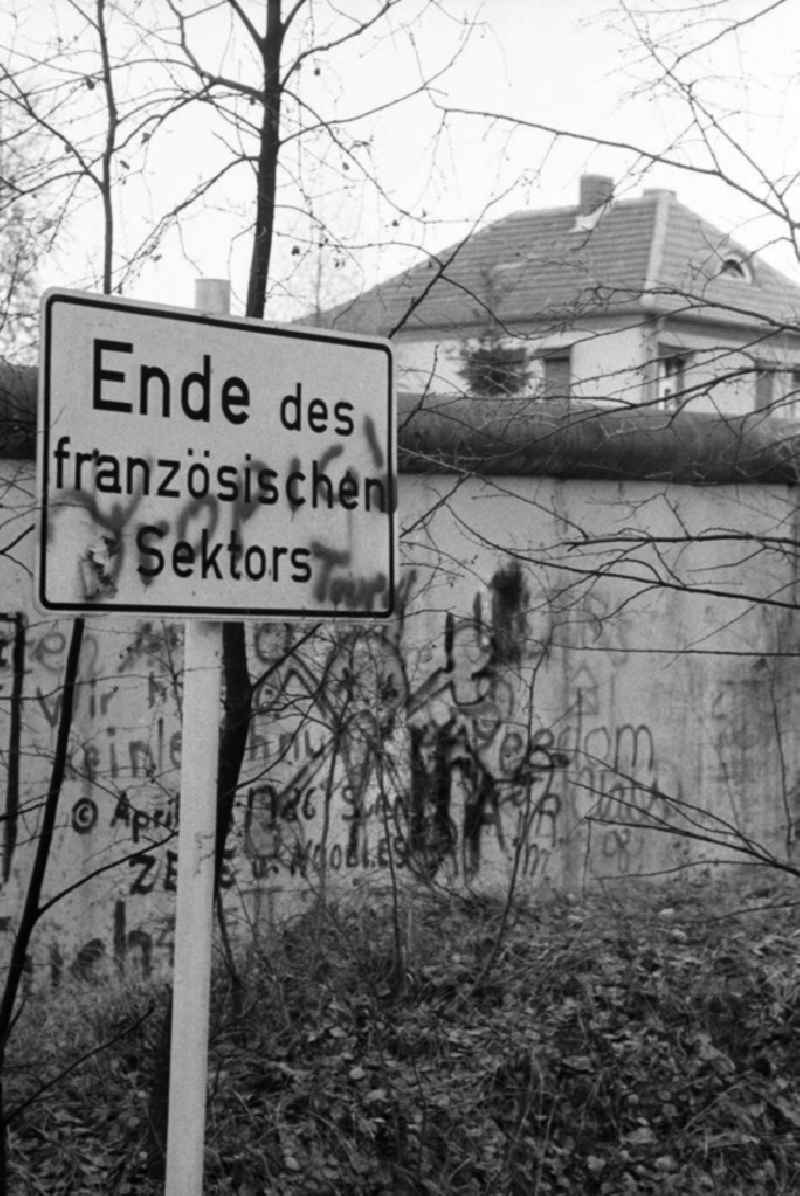 Schild vor der Grenze / Mauer der DDR mit der Aufschrift 'Ende des französischen Sektors'. Mauer und Schild mit Graffiti / Schmierereien, dahinter ein Dach eines Einfamilienhauses.