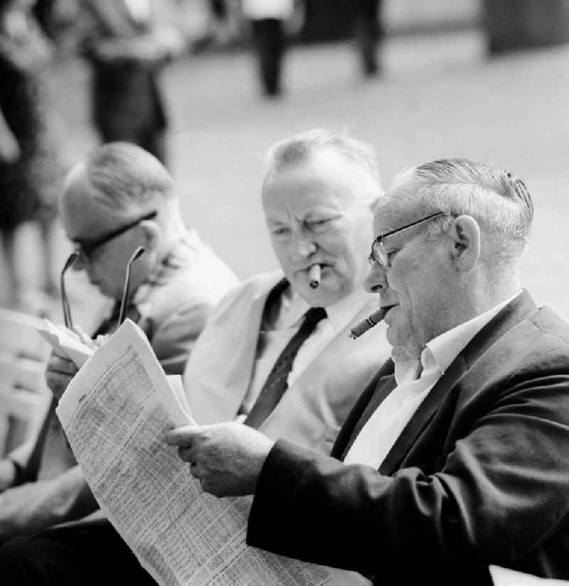 Older gentlemen with cigars in their mouths study the placements of racehorses at the Hoppegarten racecourse in Hoppegarten in the state of Brandenburg on the territory of the former GDR, German Democratic Republic
