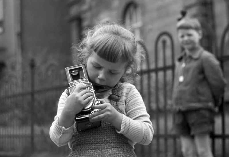 Ich kann das schon allein! - Stolz hält ein Mädchen eine Flexaret Automat Kamera der Firma Meopta in ihren Händen und versucht sich an den ersten Bildern. Der Junge im Hintergrund schaut interessiert zu.