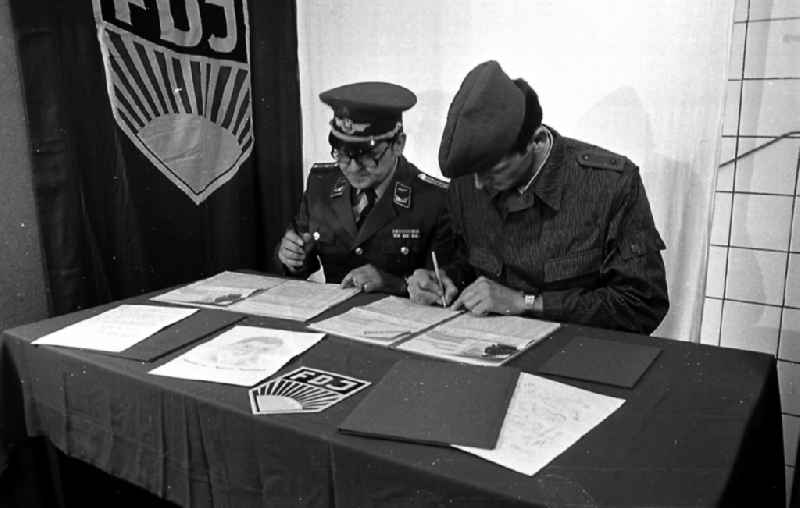 Soldier and ensign in the uniform of the LSK/LV Air Force of the FTB-9 Aviation Technical Battalion of the NVA in front of an FDJ flag at a table in Karlshagen, Mecklenburg-Western Pomerania in the area of the former GDR, German Democratic Republic