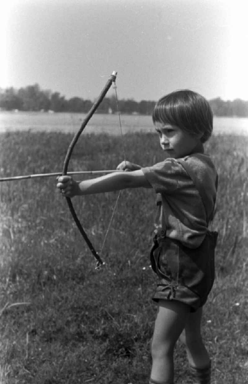A small child in leather pants playing with bow and arrow on a meadow in Brandenburg
