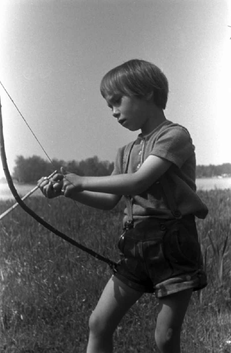 A small child in leather pants playing with bow and arrow on a meadow in Brandenburg