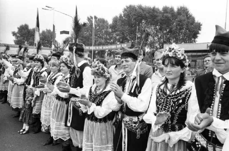 Staatsbesuch von Erich Honecker in der Volksrepublik Polen. Krakauer Bürger in Volkstrachten stehen zusammen und klatschen anlässlich zum Besuch des Staatsratsvorsitzenden der DDR Erich Honecker. Im Hintergrund Flagge DDR und Polen.