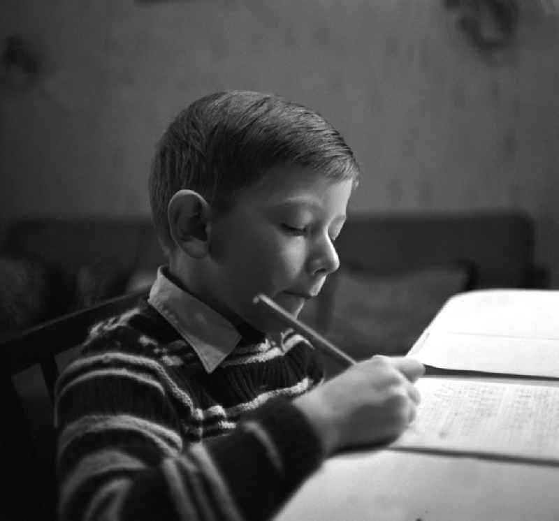 Ein Junge sitzt an einem Tisch im Wohnzimmer seines zu Hauses in Leipzig und lernt erstes Schreiben.