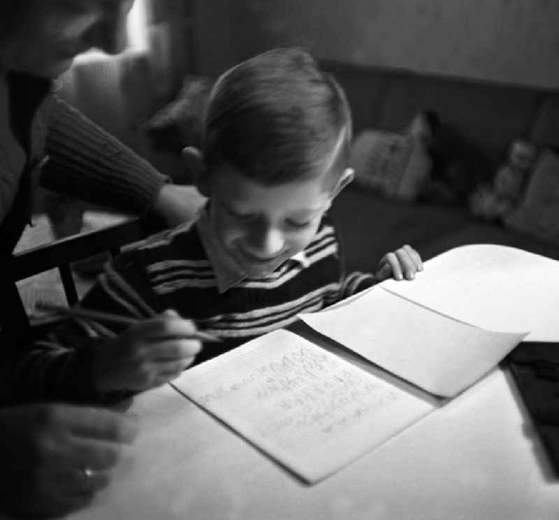 Ein Junge sitzt an einem Tisch im Wohnzimmer seines zu Hauses in Leipzig und lernt mit Hilfe seiner Mutti / Mama erstes Schreiben.