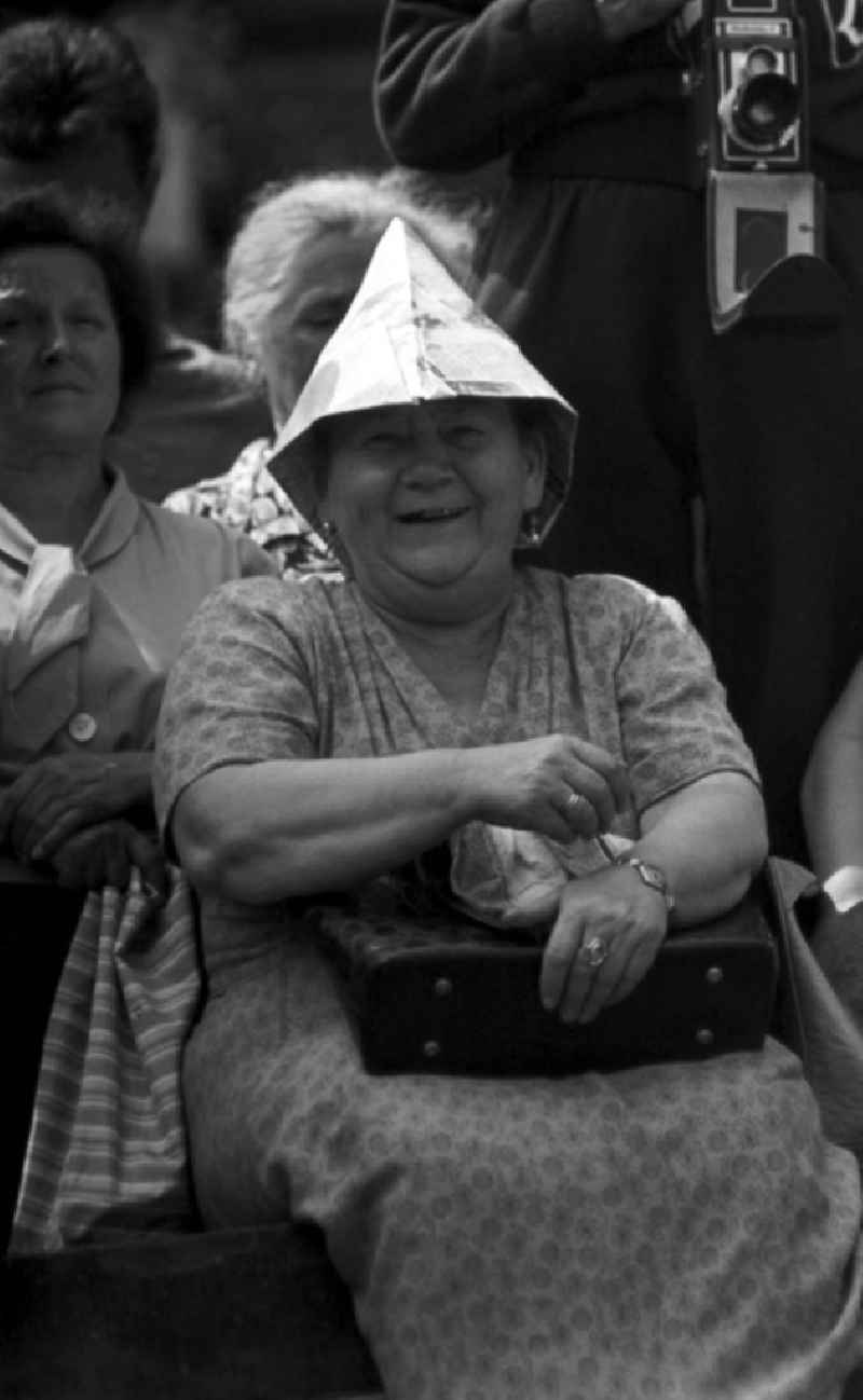 Eine Besucherin lächelt beim IV. Deutschen Turn- und Sportfest in Leipzig vom 1.-4.8.1963 in die Kamera. Ein selbstgebastelter Papierhut schützt vor der heißen Augustsonne.