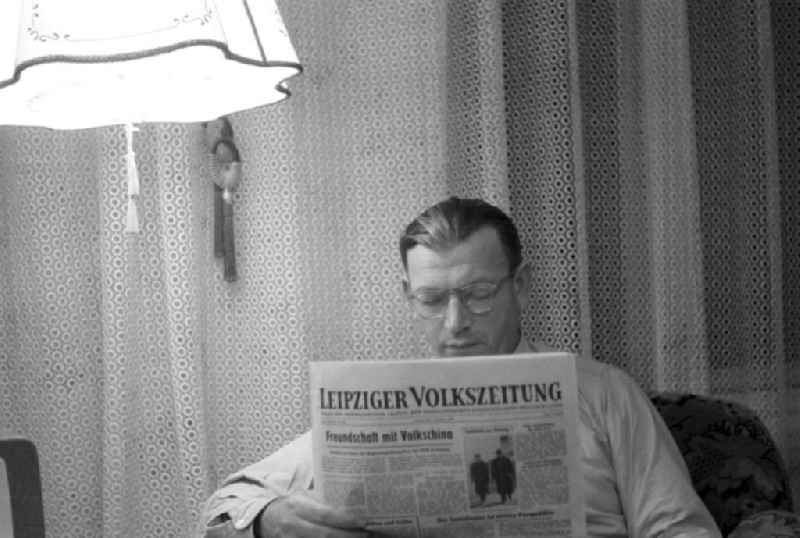 Ein Mann sitzt in seinem Wohnzimmer und liest in der Leipziger Volkszeitung die neuesten Nachrichten - Schlagzeilen wie 'Freundschaft mit Volkschina' und 'Der Sozialismus ist unsere Perspektive' prägen die Titelseite.