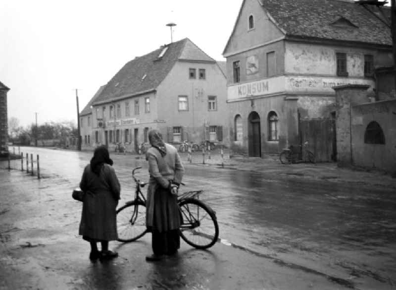Grau in grau erscheinen Konsum und 'Gasthaus zur Eisenbahn' mit bröckelnden Fassaden und verblaßten Schriftzügen in einem Dorf nahe Leipzig. Zwei Frauen mit Kopftuch stehen an der Straße.