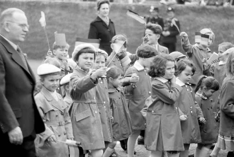 Kinder winken mit DDR-Fähnchen auf der Demonstration zum 1. Mai 1958 in Leipzig. Die Fahnen sind noch ohne das erst am 1. Oktober 1959 offiziell eingeführte DDR-Emblem aus Hammer, Zirkel und Ehrenkranz.