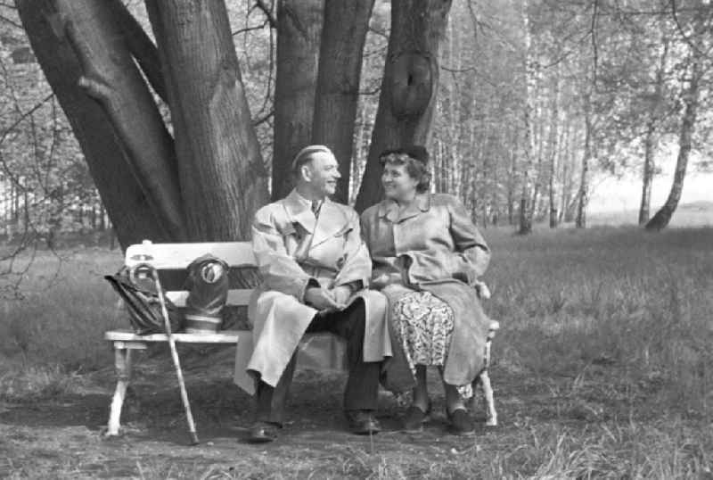 Ein älteres Paar sitzt auf einer Bank in einem Park in Leipzig und lächelt sich an.