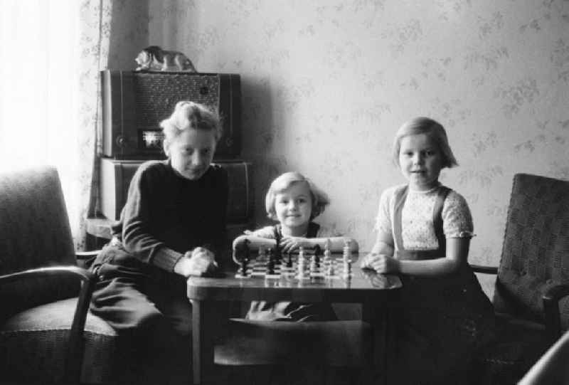 Kinder posieren am Schachtisch mit aufgebauter Schachpartie für ein Gruppenfoto in Leipzig. Im Hintergrund ein Röhrenradio.