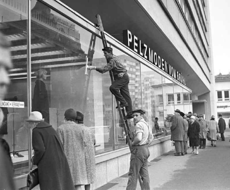 Während ältere Damen neugierig die Auslagen betrachten, reinigen zwei Fensterputzer die Schaufenster des Pelzmodengeschäftes vom Brühl in Leipzig. Das zehngeschossige Haus der Interpelz am Brühl (Hochhaus Brühlpelz) war 1966 eingeweiht worden. Dennoch errang der Brühl seinen Vorkriegsruf als Weltstraße der Pelze nicht zurück.